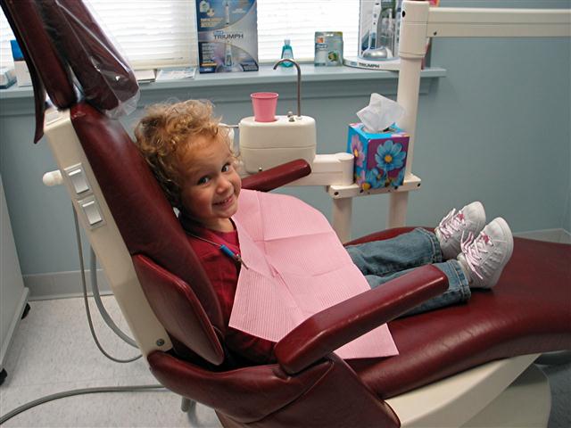 A young girl in a red shirt and blue jeans sitting in a dental chair at Terrance J. O'Keefe, DDS, LLC in Penfield, NY 