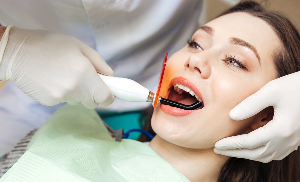 A dentists using a specific tool to clean a woman's mouth
